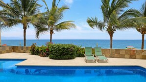 A swimming pool with lounge chairs and palm trees, overlooking the ocean.
