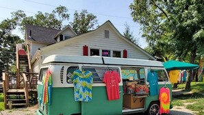 Een oldtimer bestelwagen, groen en wit, met kleurrijke handdoeken die aan de achterkant hangen, geparkeerd voor een huis.