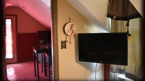 Een kamer met een aan de muur bevestigde televisie, een eettafel met stoelen en een raam met gordijnen.