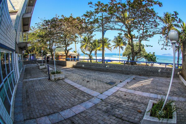 A paved walkway with benches, a view of the ocean, and palm trees.