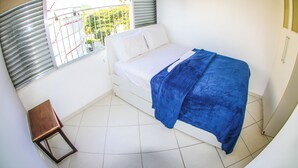 Een slaapkamer met een bed, een klein houten krukje en een raam met jaloezieën.