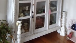 Een witte, verweerde kast met glazen deuren, gevuld met diverse borden en keramiek.