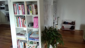 Een kamer met een witte boekenkast vol boeken, een kamerplant en een witte kast met spiegel.