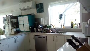 Een kleine keuken met witte kastjes, een vaatwasser en een raam met gordijnen.