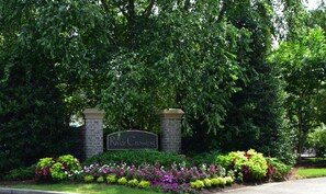 A sign with the name 'River Crossing' surrounded by lush greenery and a variety of colorful flowers. - River Crossing Apartment 1233 (North Myrtle Beach)