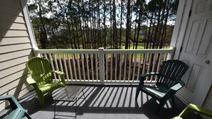 En inglasad veranda med två gröna Adirondack-stolar och ett metallbord, med utsikt över ett skogsområde.