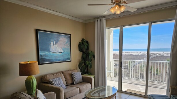 A living room with a beige sofa, a glass coffee table, a painting of sailboats, a green lamp, and a view of the beach through large windows. - Inn at Dauphin Island 310 Beautiful Unit with Wonderful Views!! (Dauphin Island)