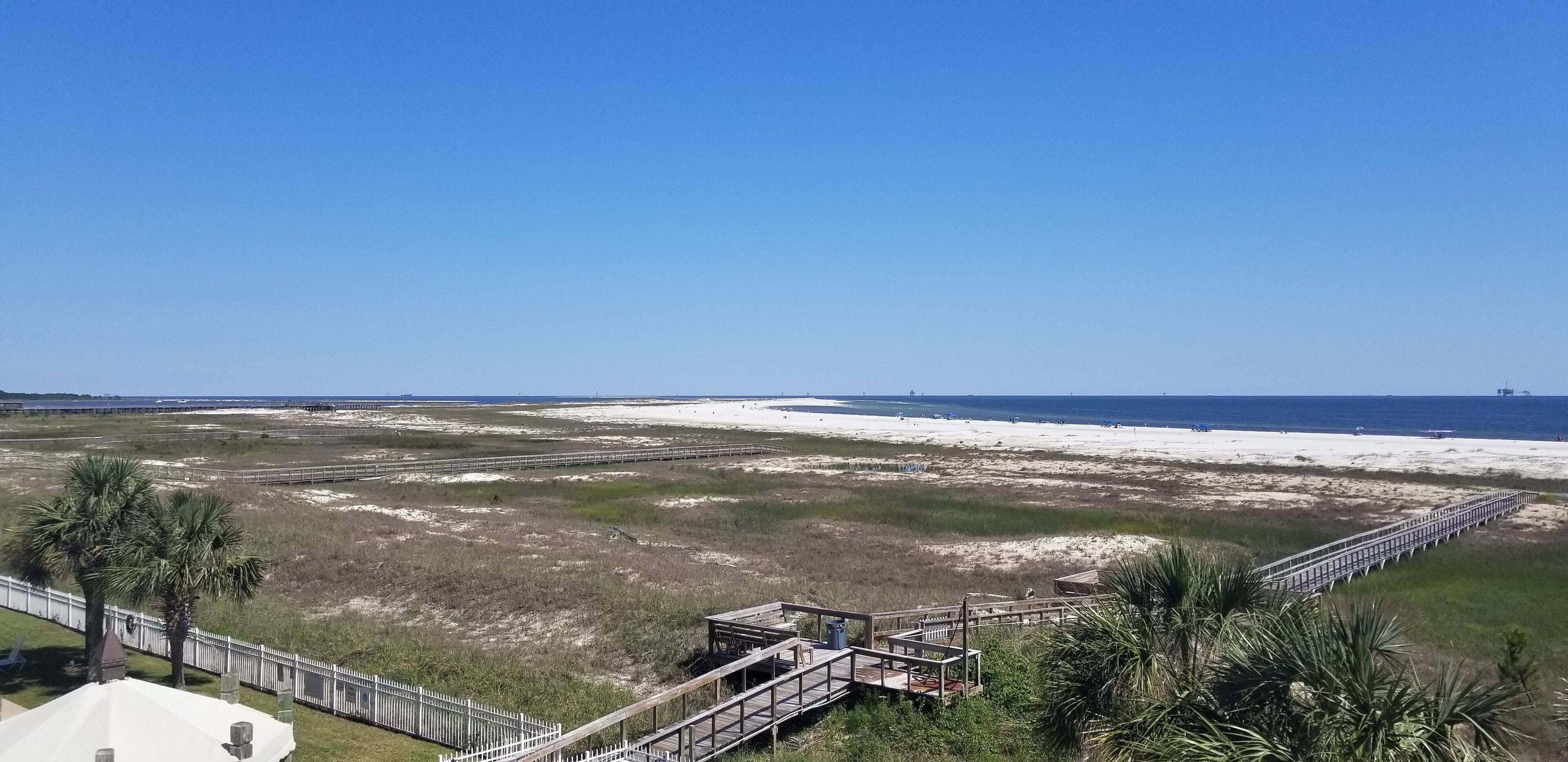 Ein Strand mit einer Holzpromenade, Palmen und wolkenlosem, blauem Himmel.