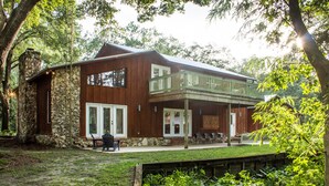 A two-story wooden cabin with a stone foundation, a balcony, and a covered patio area. - Secluded Waterfront Retreat With Private Dock                                    (Ocklawaha)