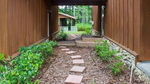 A wooden pathway leading to a covered entrance of a building, surrounded by greenery and a stone wall. - Secluded Waterfront Retreat With Private Dock                                    (Ocklawaha)