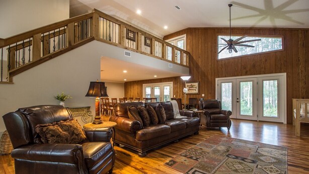 A spacious living room with a high ceiling, a wooden staircase, and a large window providing natural light. - Secluded Waterfront Retreat With Private Dock                                    (Ocklawaha)