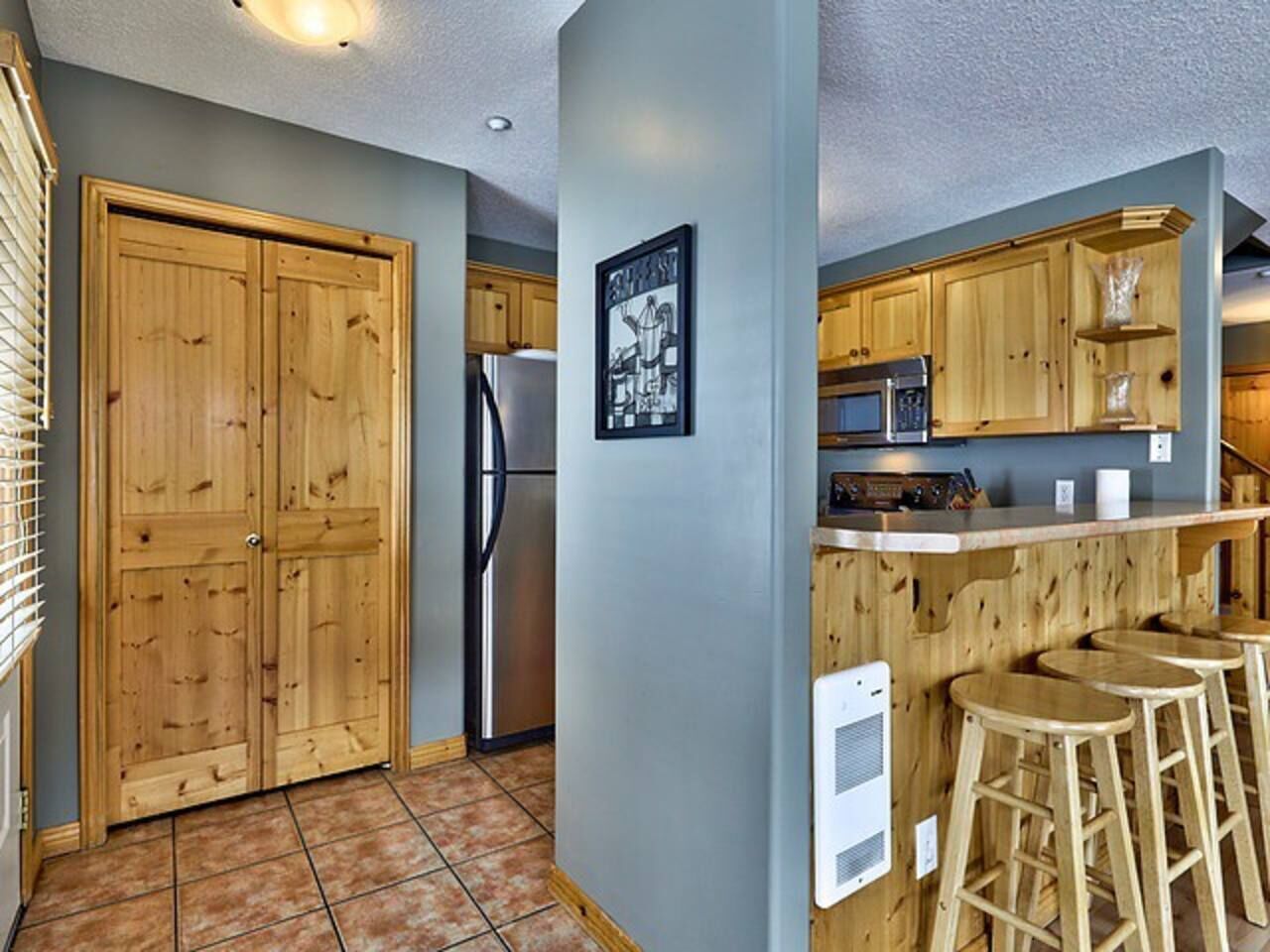 A kitchen with wooden cabinets, a stainless steel refrigerator, and a bar area with stools.