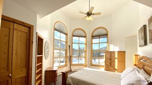 Une chambre à coucher avec un lit, une armoire en bois et un bureau. Il y a trois fenêtres donnant sur un paysage enneigé.