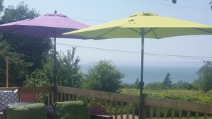 Une terrasse aménagée avec du mobilier d’extérieur, comprenant un canapé et des fauteuils, placée sous deux parasols et offrant une vue sur une étendue d’eau.