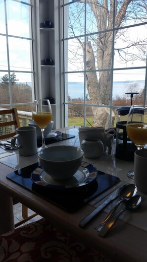 A dining table with a view of a lake and trees through large windows. - Casa Moana, Lovely old house overlooking St. Mary`s Bay, with free breakfast. (Plympton)