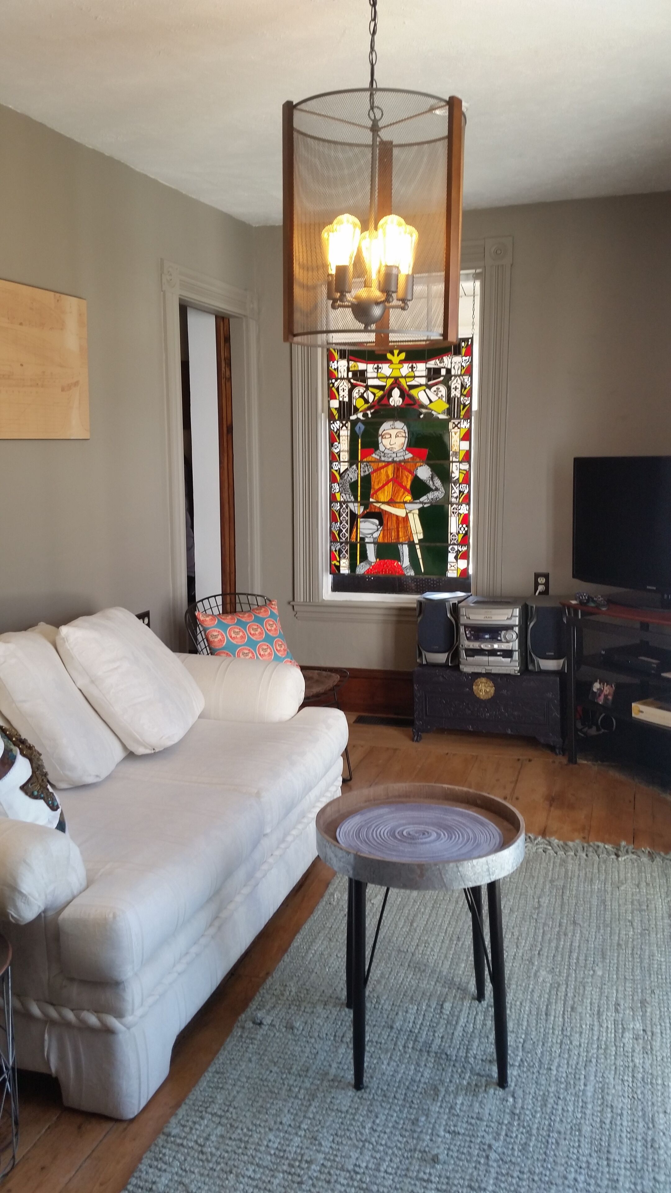 A living room with a white sofa, a round coffee table, a stained glass window, and a television.