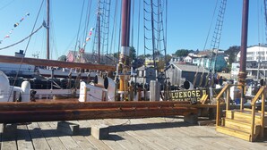Une terrasse en bois sur laquelle est fixée une plaque portant l’inscription « LUENOSE II », et un navire amarré, doté de plusieurs mâts et d’un gréement complexe.