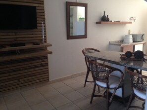 A kitchen with a wooden cabinet, a TV mounted on the wall, wicker chairs, and a small island with a table. - 3 SEA-FRONTED Houses - Beach of Mariscal, Bombinhas, SC - HOUSE #7 (Bombinhas)