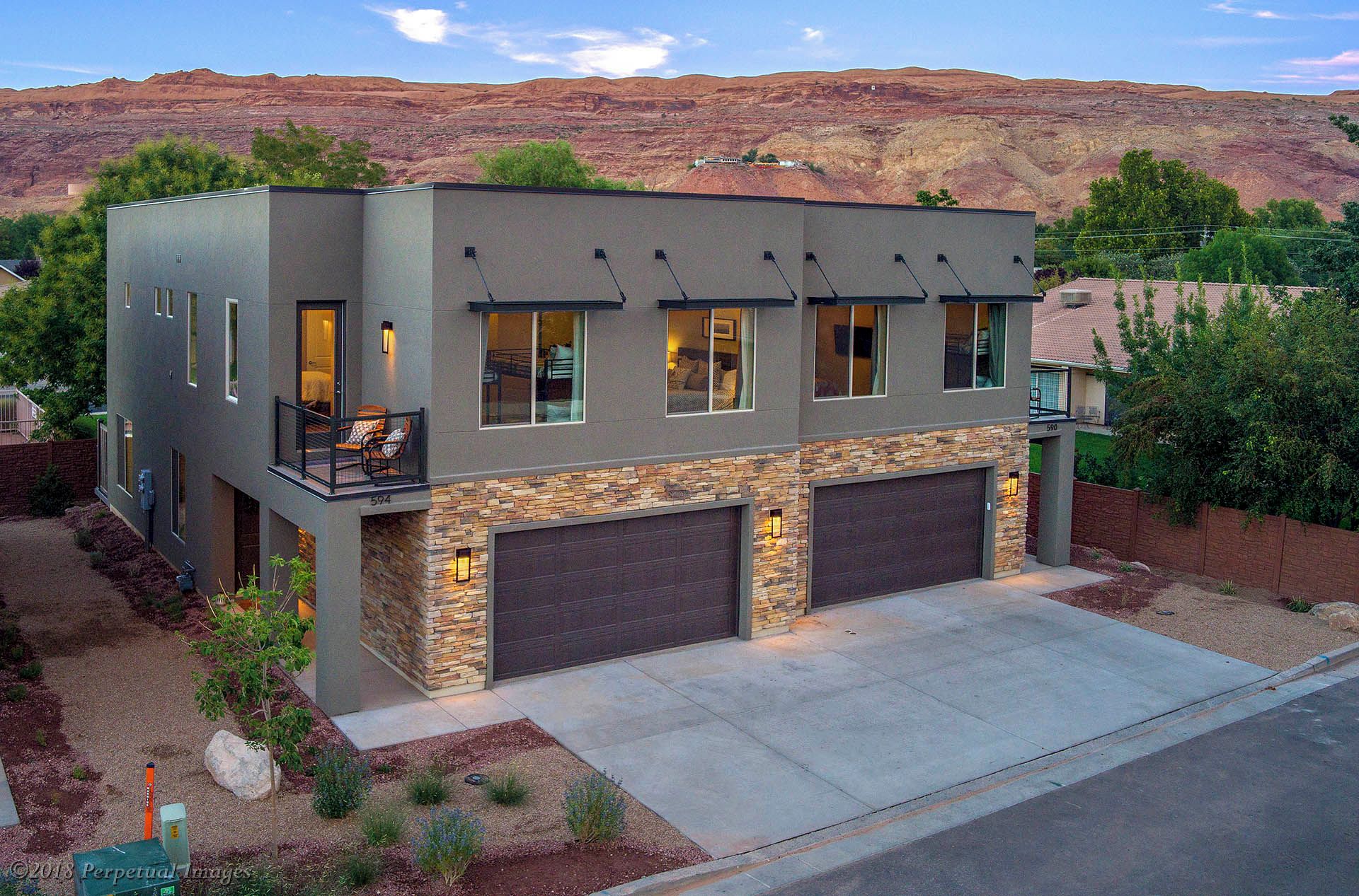 A modern two-story house with a stone facade, two garages, and a balcony with outdoor seating.