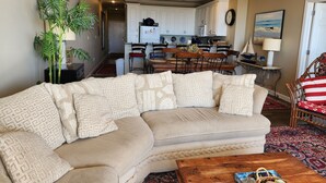 Una sala de estar con un sofá seccional color beige, una mesa de centro de madera, y un comedor con una mesa y sillas de madera.