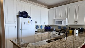 Una cocina con armarios blancos, encimera de granito, refrigerador, microondas y estufa.
