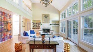 A spacious living room with a fireplace, large windows, and a high ceiling. - Wainscott Southampton Estate Timeless luxury with a private pool,... (Wainscott)