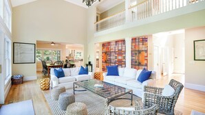 A spacious living room with a high ceiling, a balcony, and a kitchen in the background. - Wainscott Southampton Estate Timeless luxury with a private pool,... (Wainscott)