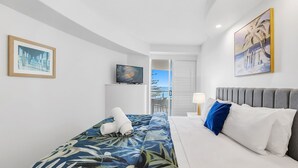 Habitación de hotel moderna con cama, televisor y balcón con vista al mar.