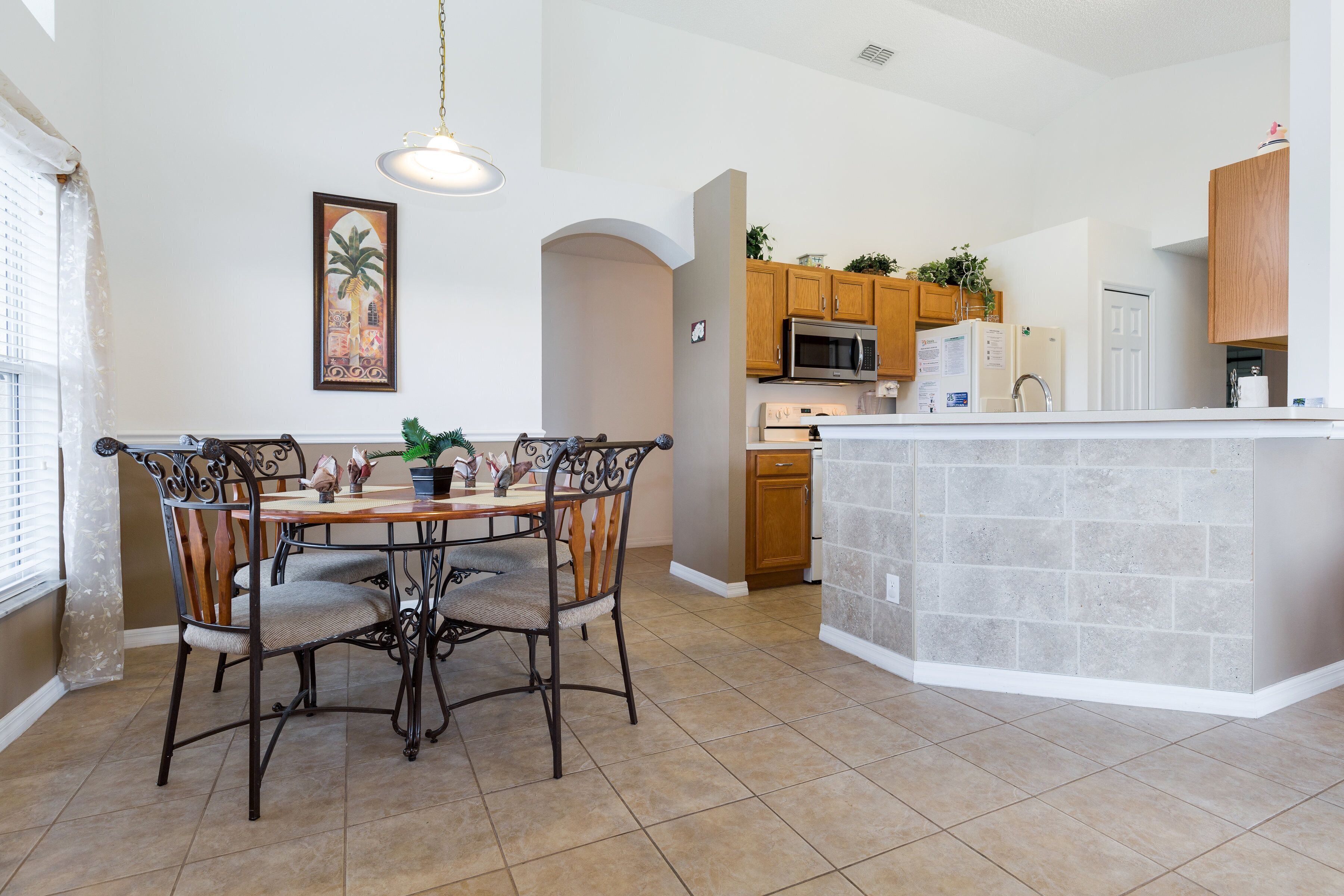 A kitchen with a dining area, featuring a central island, wooden cabinets, and a tiled floor.