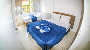 Une chambre avec un grand lit, un plus petit lit et une fenêtre avec des stores.