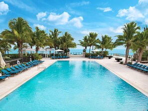 A swimming pool with blue lounge chairs and palm trees, surrounded by a clear sky.
