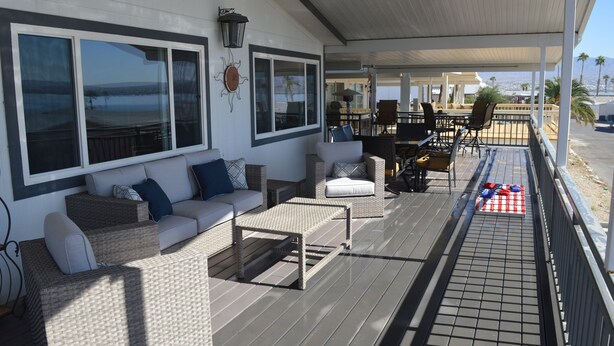 A covered outdoor seating area with wicker furniture, a small table, and a view of the ocean. - Major's Toy Box - Amazing Home Havasu Landing  (Havasu Lake)