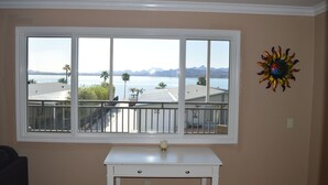A room with a large window overlooking a body of water and mountains, a white table, and a decorative sun-like object on the wall. - Major's Toy Box - Amazing Home Havasu Landing  (Havasu Lake)