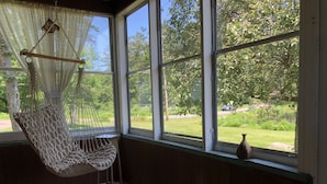 A room with a hammock chair by a large window overlooking a garden. - Adirondack Cottage - Four Season, Pet-Friendly, Cozy & Beautiful. Read  reviews! (Lowville)