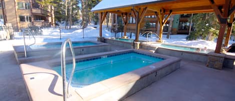 A pool area with two rectangular pools, wooden deck, and a covered seating area.