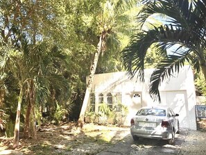 Un edificio blanco con puerta de garaje, rodeado de palmeras y un coche estacionado.