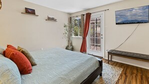 Un dormitorio con cama, un banco, una planta en maceta y un televisor en la pared.