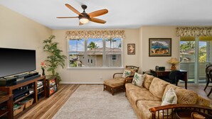 A living room with a TV, wooden entertainment unit, sofa, and chairs. - Princeville Condo with AC, Pool, Garage, Beach Gear 27B (Princeville)