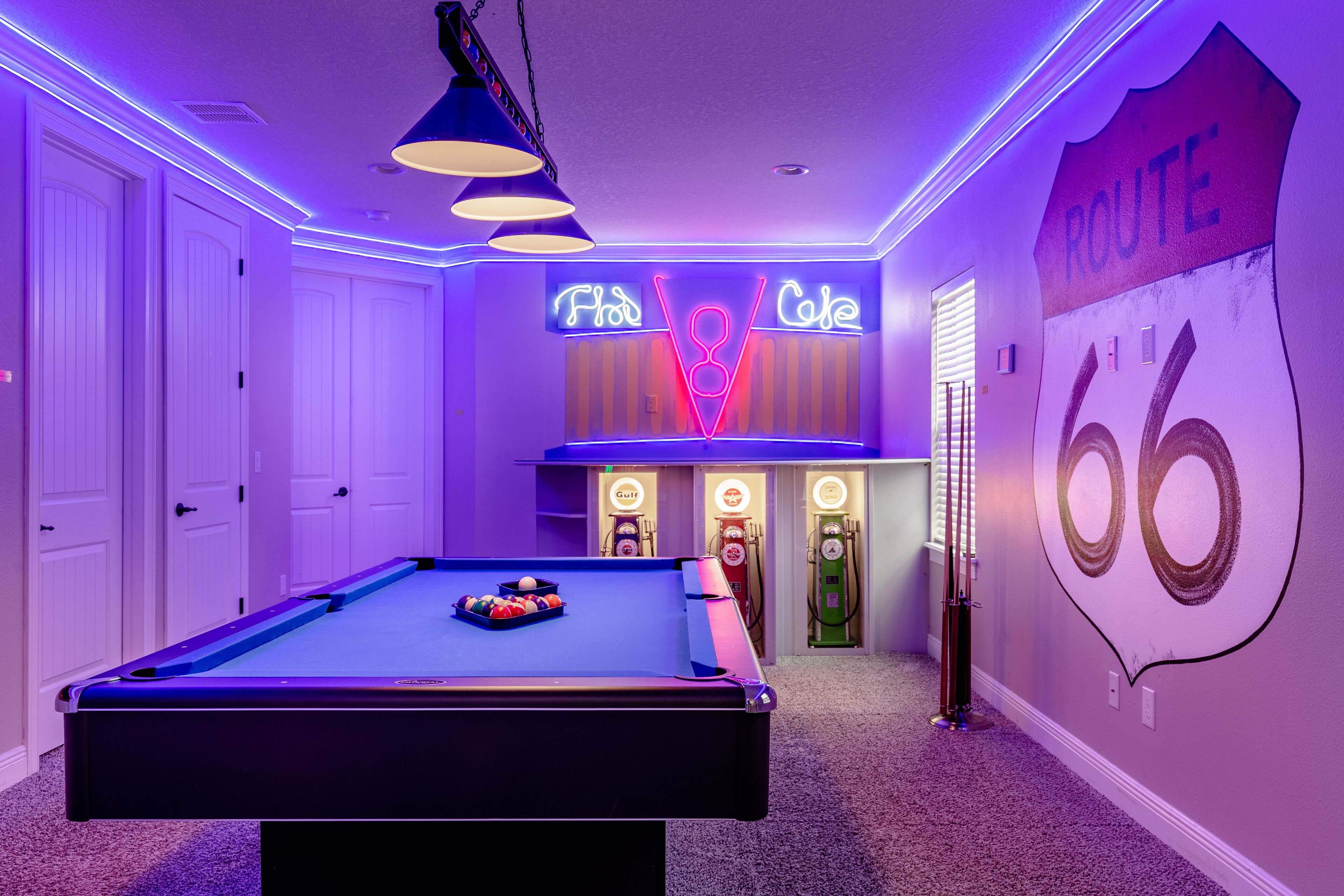 A pool table in a room with neon signs and a vintage Route 66 mural.