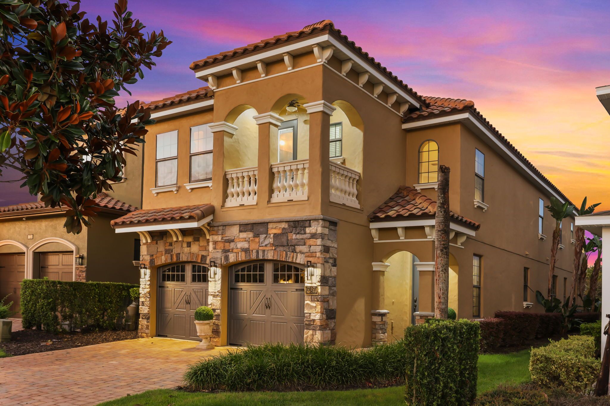 A two-story house with a stone facade, multiple garage doors, and a well-maintained front yard.