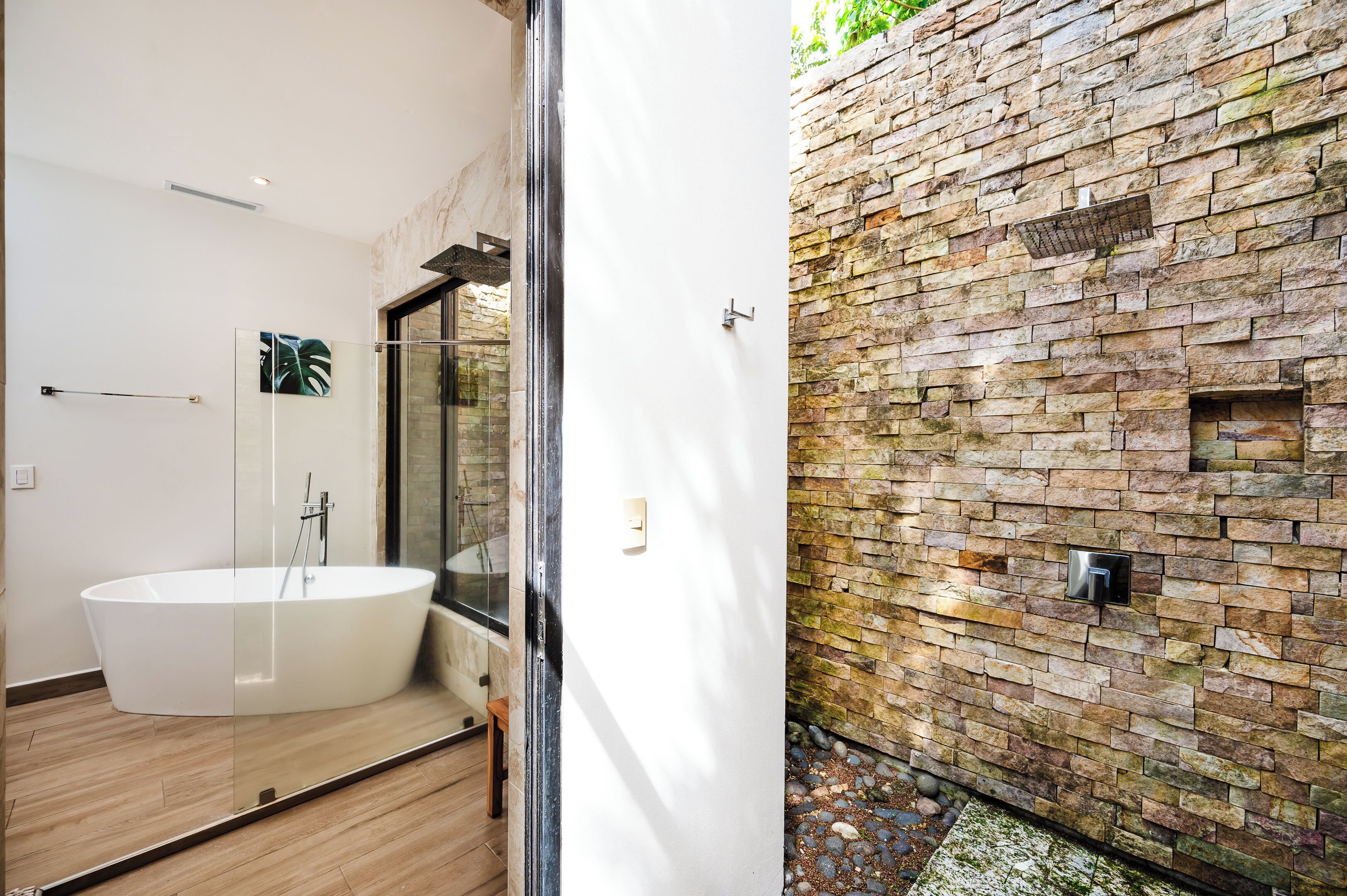 A modern bathroom with a freestanding bathtub, a glass shower enclosure, and a stone wall.