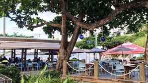Un espace extérieur aménagé pour les repas, avec des tables et des chaises, un coin salon abrité et une vue sur l’eau.