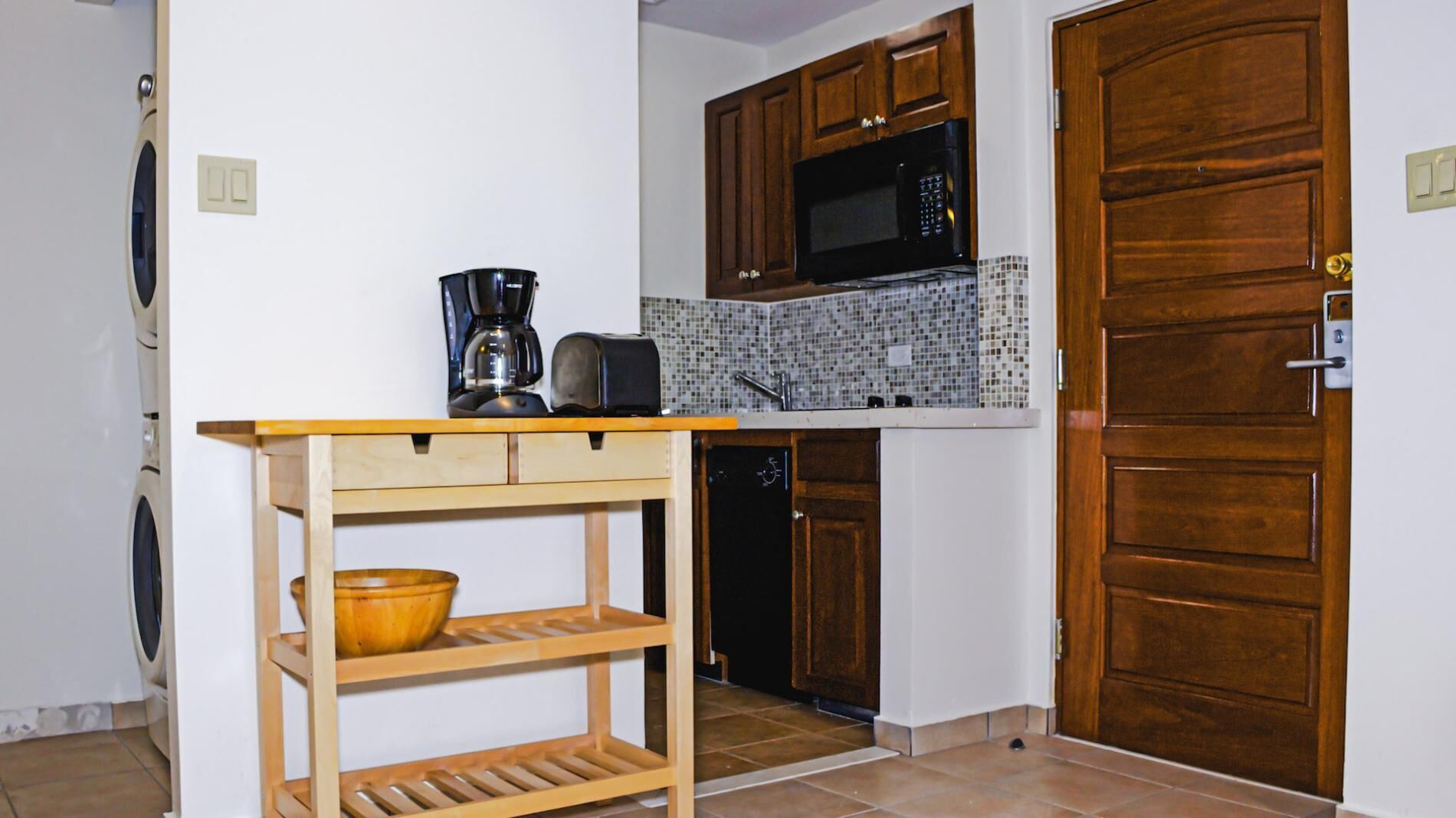 A compact kitchen with wooden cabinets, a microwave, a coffee maker, and a dishwasher.