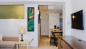 Un salon moderne comprenant un canapé, une petite table avec une lampe, et un coin cuisine avec une table à manger et des tabourets de bar.
