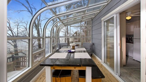 Un invernadero con una mesa y sillas, ventanas amplias y vista a árboles.