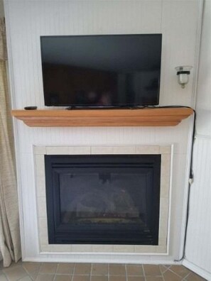 Une cheminée surmontée d’un téléviseur, un luminaire fixé au mur et une porte sur le côté droit.