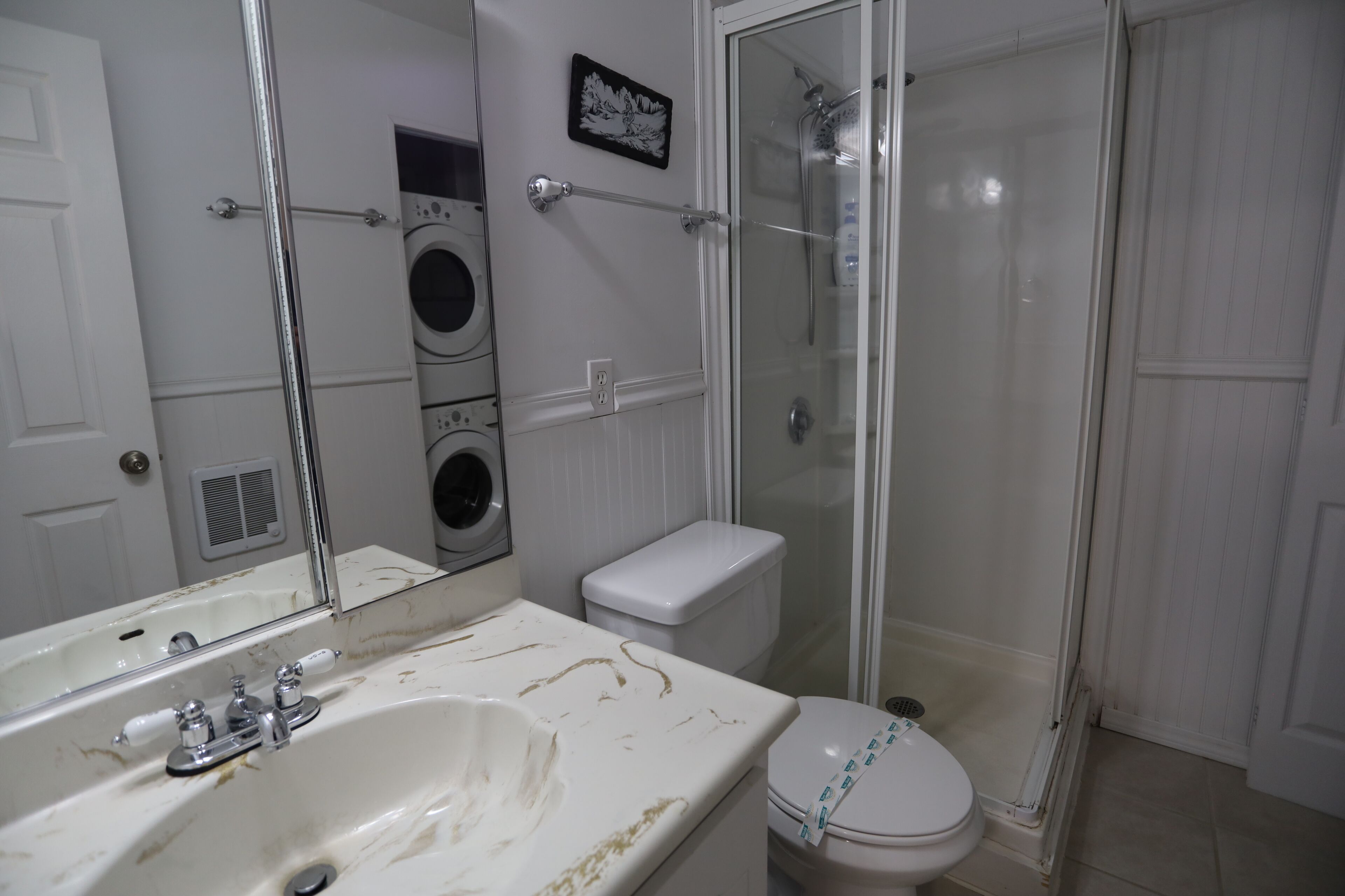 A bathroom with a sink, toilet, shower, and a mirror.