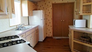 A compact kitchen with a gas stove, white refrigerator, and a microwave on the countertop.