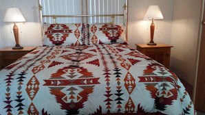 A bed with a patterned bedspread, two bedside tables with lamps, and a window with blinds.