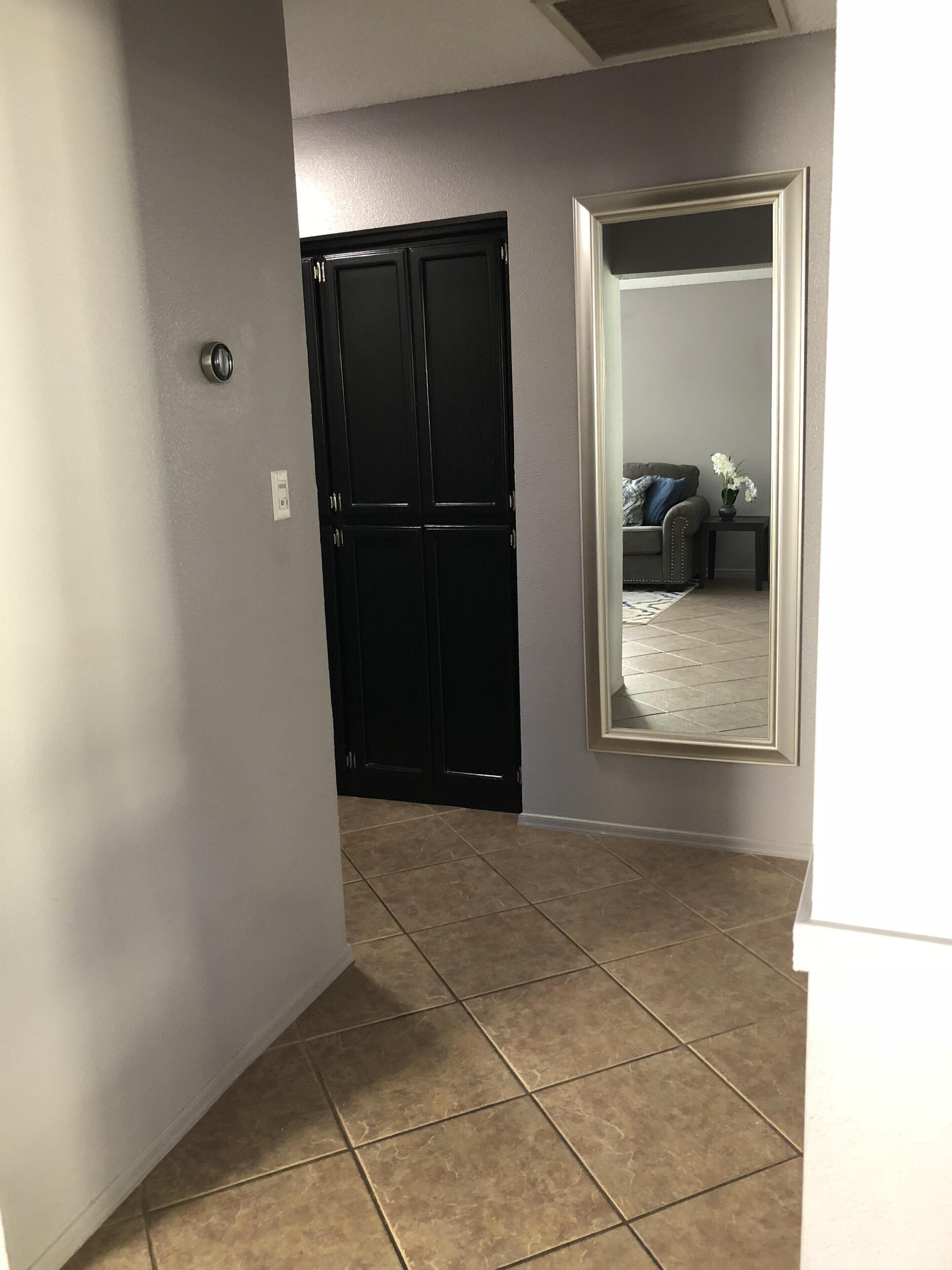 A hallway with a black door, a white wall, and a tiled floor.